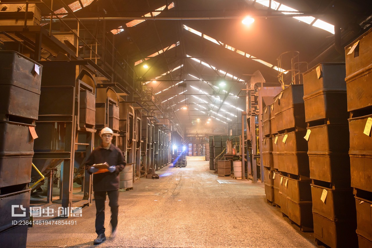 Worker walking past crates of steel shot in steel foundry